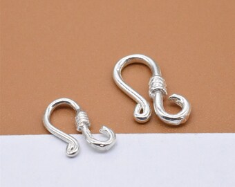 May include: Two silver-toned metal clasps for jewelry making. The clasps are shaped like a hook with a small loop at the top.