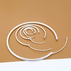 May include: A set of silver hoop earrings of varying sizes. The hoops are arranged in a circular pattern, with the largest hoop in the center and the smallest hoop on the outside.