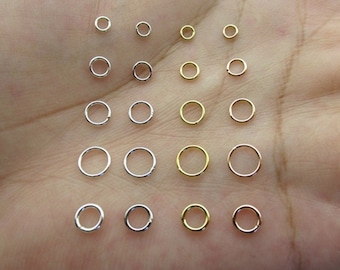 May include: A collection of small, silver and gold jump rings of various sizes. The rings are arranged in rows on a hand.