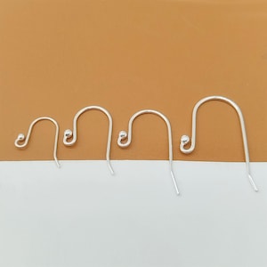 May include: Four silver-colored earring hooks of varying sizes are displayed against a brown background. Each hook features a curved design with a small, rounded bead at the top and a slender, downward-pointing wire.