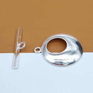 May include: Silver-toned metal toggle clasp with a round loop on one end and a round, open-circle design on the other end. The clasp is used for jewelry making.