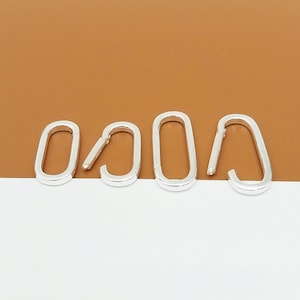 May include: Four silver oval carabiner clasps. One clasp is open, showing the hinge. The clasps are set against a white and brown backdrop. These clasps are suitable for jewellery making or craft projects.
