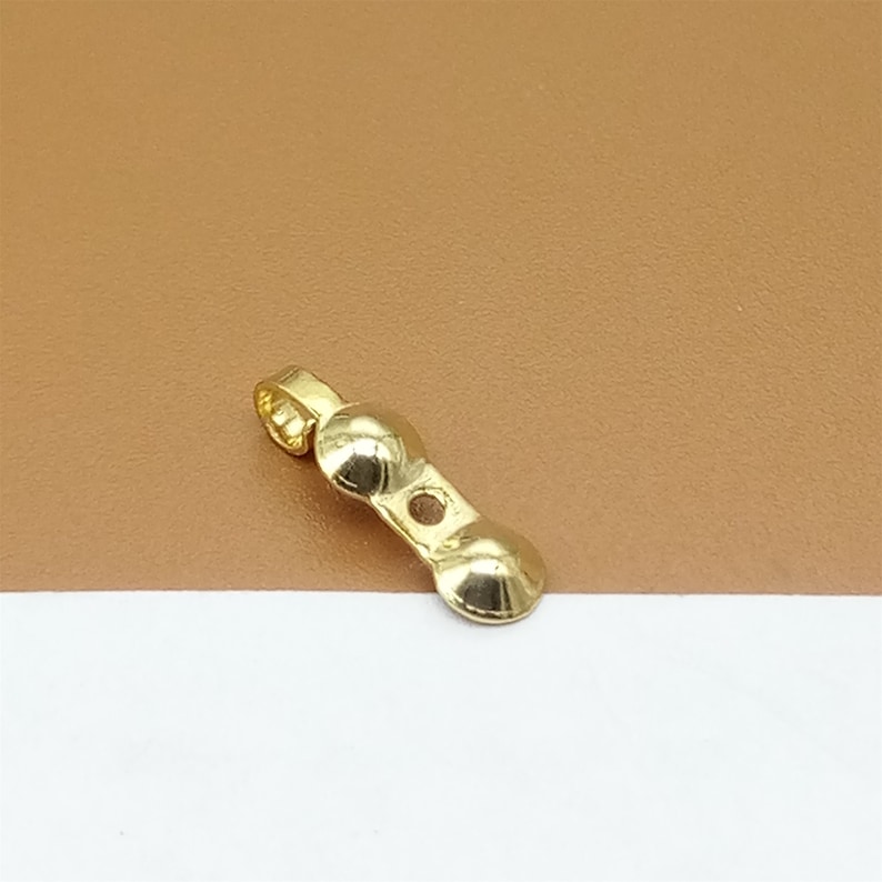 May include: Gold-toned metal jewelry finding with a loop at one end and two rounded, slightly domed sections. The finding has a small hole in the center.