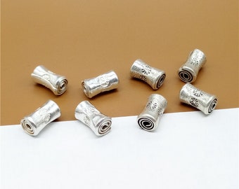 May include: Eight silver-toned metal beads with a decorative scroll design. The beads are cylindrical and have a slightly rounded shape.