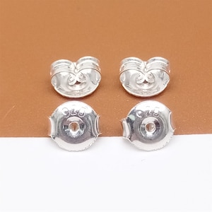 May include: Four silver earring backs, two with a decorative design and two with a smooth, round surface. The backs are marked with the number "925".