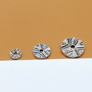 May include: Three silver metal round beads with a textured surface and a hole in the centre. The beads are different sizes.