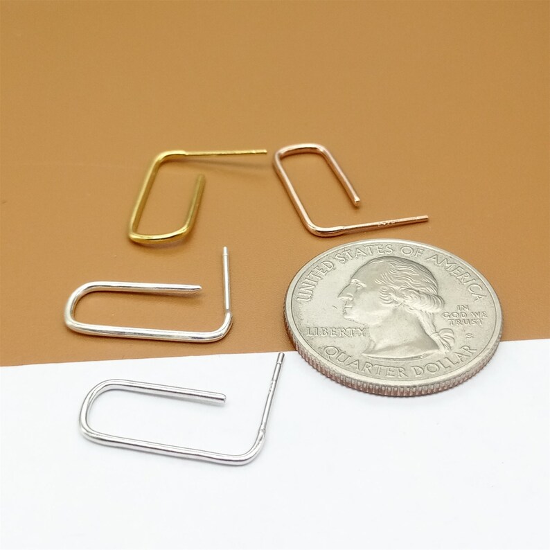 May include: Four small hoop earrings, two gold and two silver, are arranged on a white surface next to a US quarter. The earrings are all about the size of the quarter.