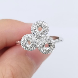 May include: A silver ring featuring three circular settings, each encrusted with small, sparkling stones. The ring's design is modern and elegant, with a focus on the intricate details of the settings.