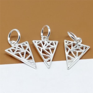 Puede incluir: Tres dijes triangulares de plata con un diseño geométrico. Los dijes tienen un bucle en la parte superior para sujetarlos a un collar o pulsera.