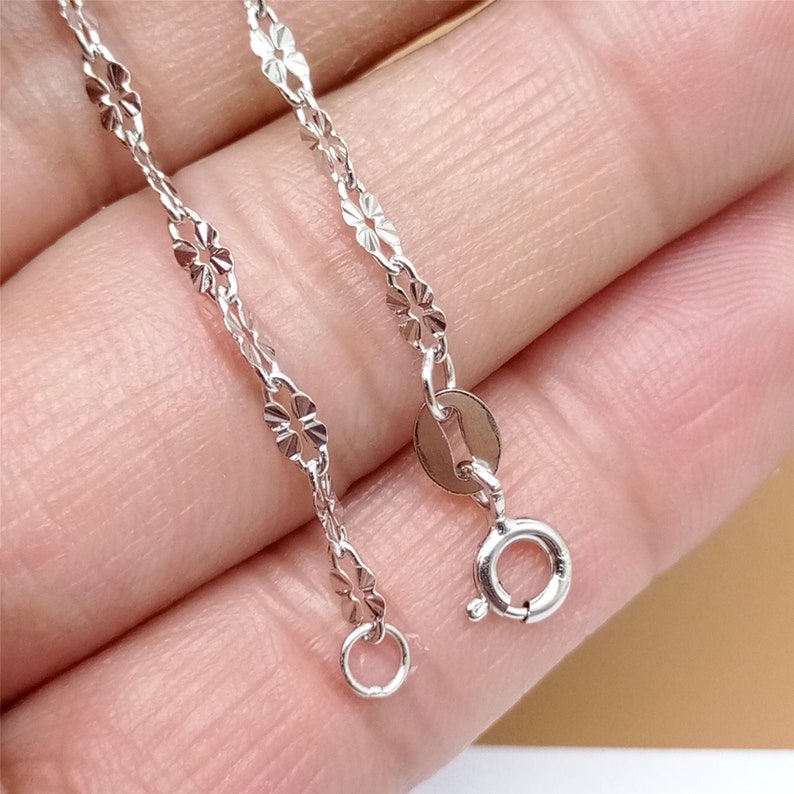 May include: A silver chain necklace with a delicate, patterned design. The chain has a lobster clasp closure.