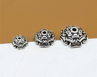 May include: Three silver-toned metal flower-shaped bead caps of varying sizes. The caps have a hole in the center for stringing.