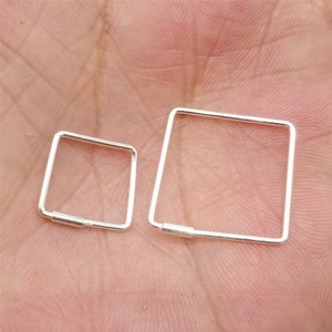 Op de afbeelding: Twee zilveren vierkante oorringen in verschillende maten. De grotere oorring is ongeveer 2,5 cm in diameter en de kleinere oorring is ongeveer 1,25 cm in diameter.