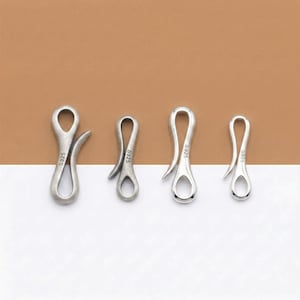 Puede incluir: Cuatro cierres plateados en forma de S de diferentes tamaños. Cada cierre tiene un lazo en la parte superior y un gancho curvo en la parte inferior. Los cierres están dispuestos sobre un fondo de dos tonos marrón y blanco.