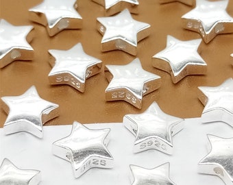 May include: A group of silver star-shaped beads, each with a 925 stamp. The beads are scattered on a brown surface.