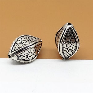 May include: Two silver-toned metal beads with an intricate swirl design. The beads are shaped like a teardrop and have a hole at the top for stringing.