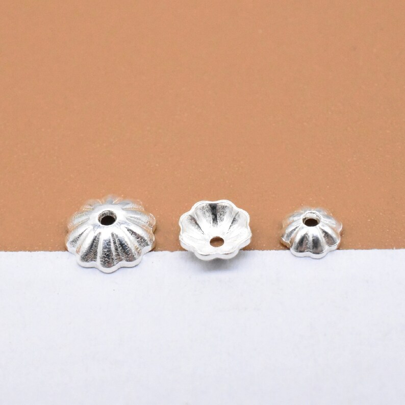 Op de afbeelding: Drie zilverkleurige metalen kralencaps in verschillende maten. De caps hebben een gegolfde rand en een klein gaatje in het midden.