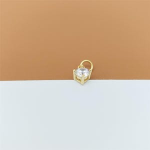 以下が含まれることがあります： 4本の爪で留められた、透明でファセットカットされた丸い宝石が特徴のゴールドトーンのメタルチャーム。チャームの上部には取り付け用の小さな円形の丸カンが付いており、磨き上げられた光沢のある仕上げが施されています。