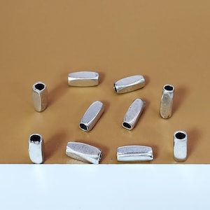 Könnte beinhalten: Zehn silberfarbene Metall-Fassperlen-Abstandshalter. Die Perlen sind oval geformt und haben eine glatte, leicht strukturierte Oberfläche.