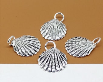 Könnte beinhalten: Vier silberfarbene Muschelanhänger mit strukturierter Oberfläche und einer kleinen Schlaufe oben zum Befestigen an Schmuck. Die Anhänger sind auf einem braunen Hintergrund angeordnet. Das Muscheldesign ist detailliert und realistisch.