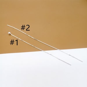 Könnte beinhalten: Zwei silberne Kettenohrringe, einer mit einer kleinen Kugel am Ende und der andere mit einem geraden Ende. Die Ohrringe sind mit #1 und #2 gekennzeichnet.