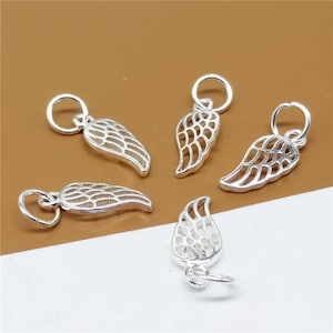 May include: Five silver angel wing charms with a delicate openwork design. The charms have a loop at the top for attaching to jewelry.