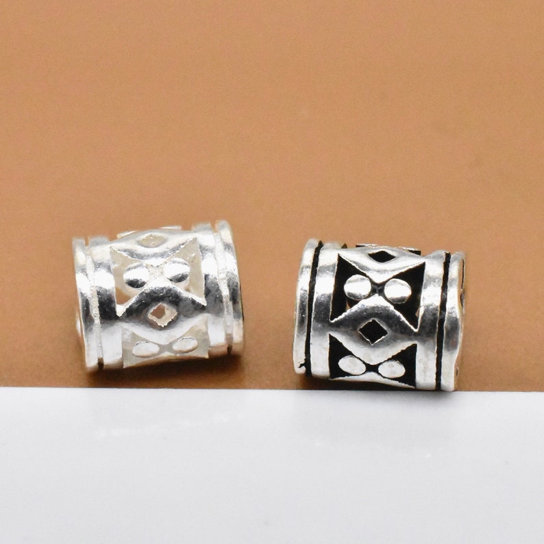 May include: Two silver-toned metal beads with an intricate geometric design. One bead has a black enamel fill, while the other is left unfilled.