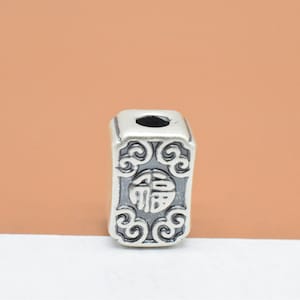May include: Silver charm with a square shape and intricate design. The charm features a Chinese character in the center and a decorative border.