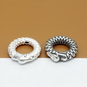 Könnte beinhalten: Zwei silberne Ringe mit Schlangenmotiv. Ein Ring ist aus poliertem Silber, der andere aus oxidiertem Silber.