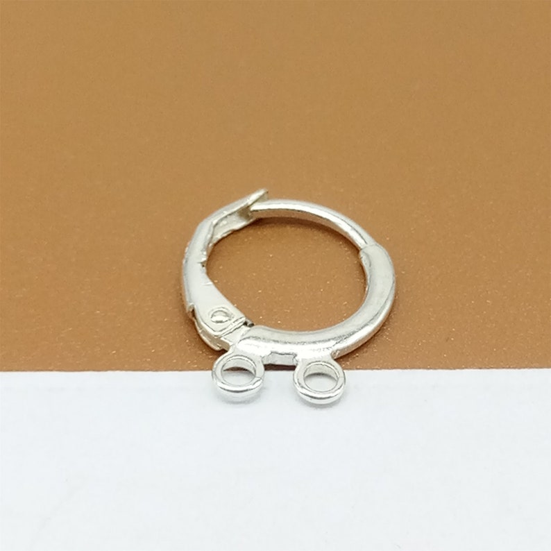 May include: Silver earring finding with a hinged hoop and two jump rings. The hoop is open and the jump rings are attached to the hoop.