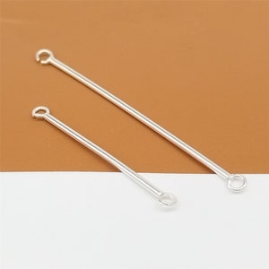 Pode incluir: Dois pinos de cabeça prateados com laços em ambas as extremidades. Os pinos de cabeça têm comprimentos diferentes.