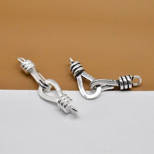 May include: Two silver-toned metal clasps with a twisted rope design. The clasps are open and ready to be attached to a necklace or bracelet.