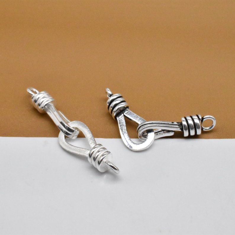 May include: Two silver-toned metal clasps with a twisted rope design. The clasps are open and ready to be attached to a necklace or bracelet.