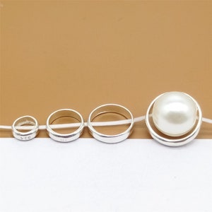 Könnte beinhalten: Vier silberne Ringe mit einer Perle in der Mitte. Die Ringe sind unterschiedlich groß und haben eingeprägte Zahlen.