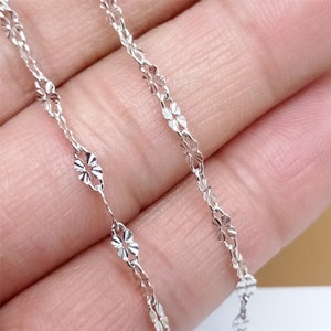 May include: A silver chain necklace with a delicate flower design. The chain is made of small, interconnected links that create a delicate and feminine look.