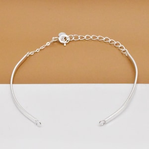 May include: A silver bangle bracelet with a delicate chain and a lobster clasp closure.
