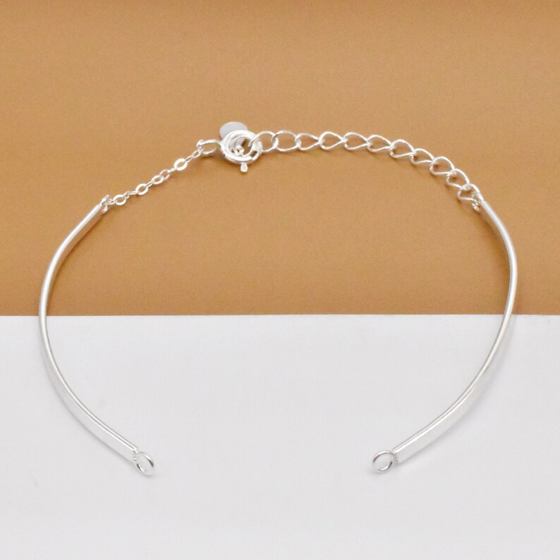 May include: A silver bangle bracelet with a delicate chain and a lobster clasp closure.