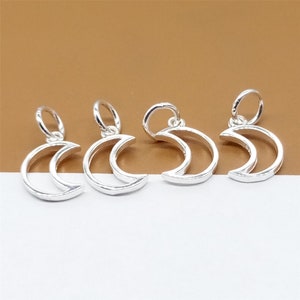 May include: Four silver crescent moon charms with a loop for attaching to jewellery. The charms are on a brown and white surface.