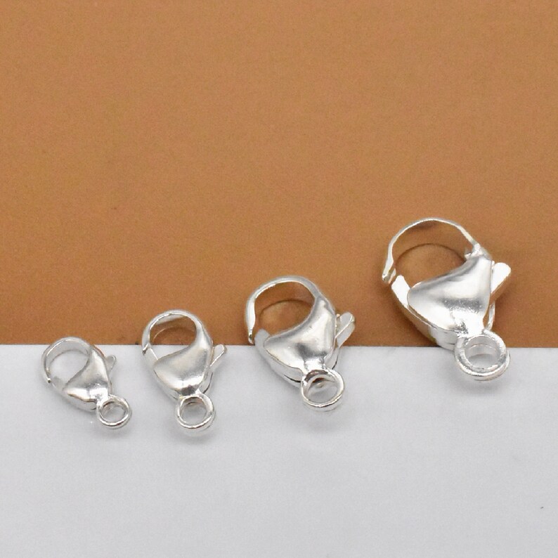 K&ouml;nnte beinhalten: Vier silberne Karabinerverschl&uuml;sse in verschiedenen Gr&ouml;&szlig;en. Die Verschl&uuml;sse sind ein beliebtes Schmuckzubeh&ouml;r f&uuml;r Halsketten, Armb&auml;nder und andere Schmuckprojekte.