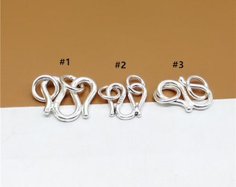 Könnte beinhalten: Drei silberfarbene Verschlüsse, mit #1, #2 und #3 beschriftet, werden vor einem braunen Hintergrund gezeigt. Jeder Verschluss hat ein anderes Design mit einer Schlaufe und einem Haken.