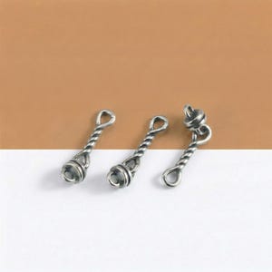 May include: Three silver-colored, twisted metal charms with a loop at one end and a decorative bead at the other. The charms are arranged on a white and brown background. The design features a spiral pattern on the stem.