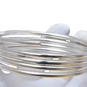 May include: A set of five silver bangle bracelets stacked on top of each other. The bracelets are all smooth and shiny.