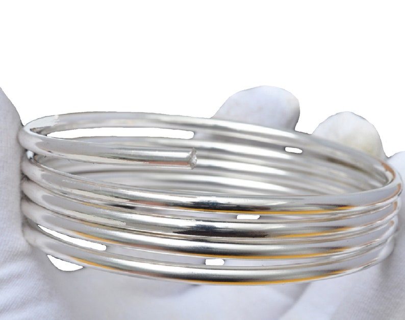 May include: A set of five silver bangle bracelets stacked on top of each other. The bracelets are all smooth and shiny.