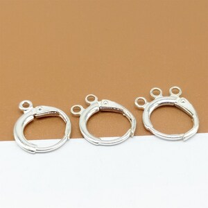 May include: Three silver-toned jump rings with three loops on each ring. The rings are on a brown surface.