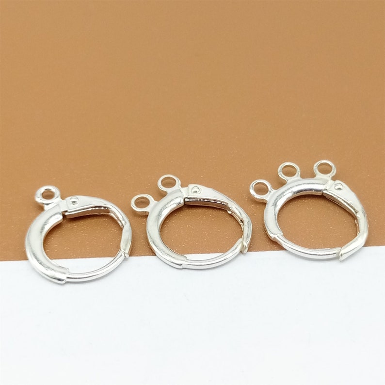 May include: Three silver-toned jump rings with three loops on each ring. The rings are on a brown surface.