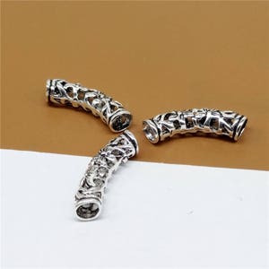 May include: Three silver-toned metal hair tie ends with an intricate, ornate design. The hair tie ends are shaped like a tube with a decorative pattern.
