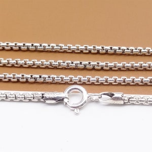 May include: A silver chain necklace with a lobster clasp. The chain is made of small, square links.