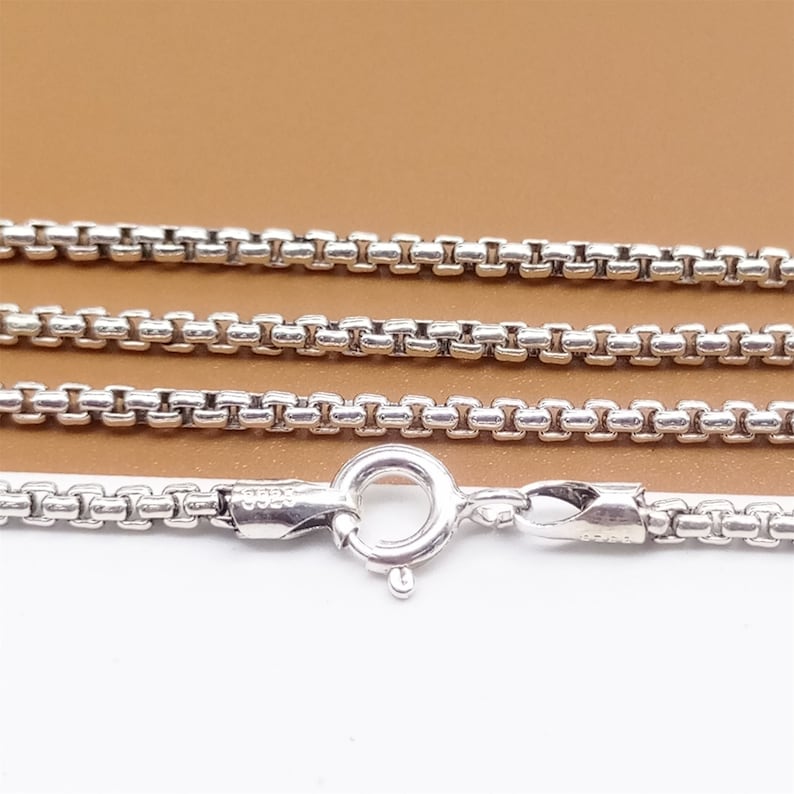 May include: A silver chain necklace with a lobster clasp. The chain is made of small, square links.