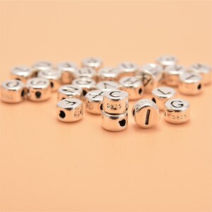 May include: A close-up of silver letter beads with the letters C, I, and G visible. The beads are marked with "S925" on the side.