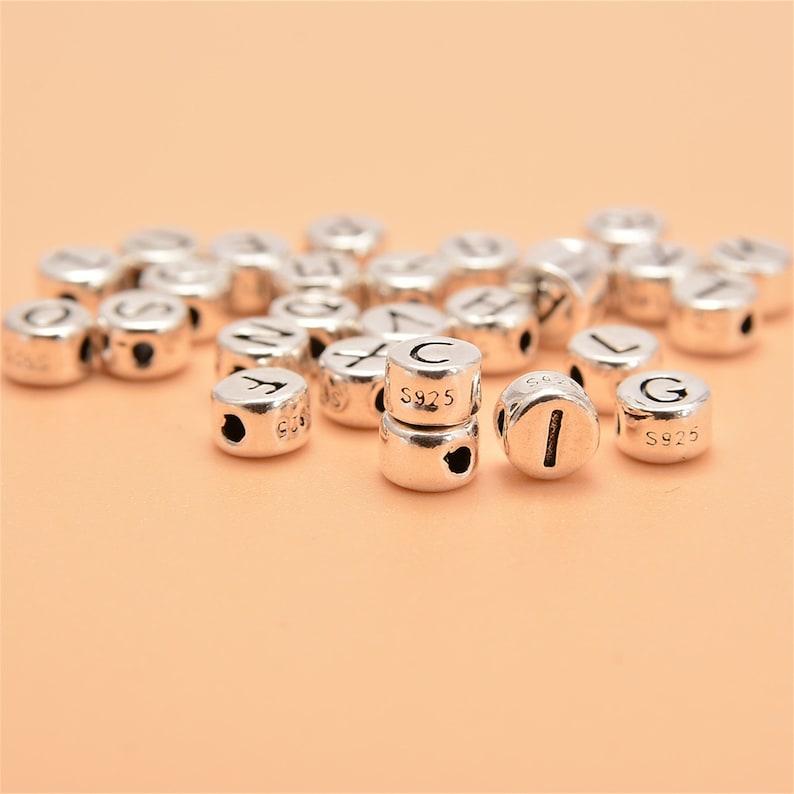May include: A close-up of silver letter beads with the letters C, I, and G visible. The beads are marked with "S925" on the side.