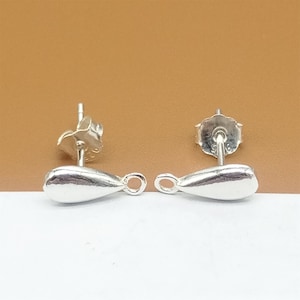 Könnte beinhalten: Ein Paar silberne Ohrringrohlinge in Tropfenform mit Sprungringen. Die Ohrringstecker sind silberfarben und haben einen Schmetterlingsverschluss.